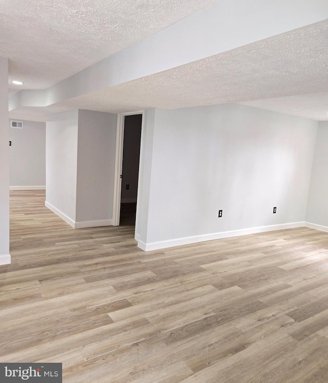 basement featuring light hardwood / wood-style floors and a textured ceiling