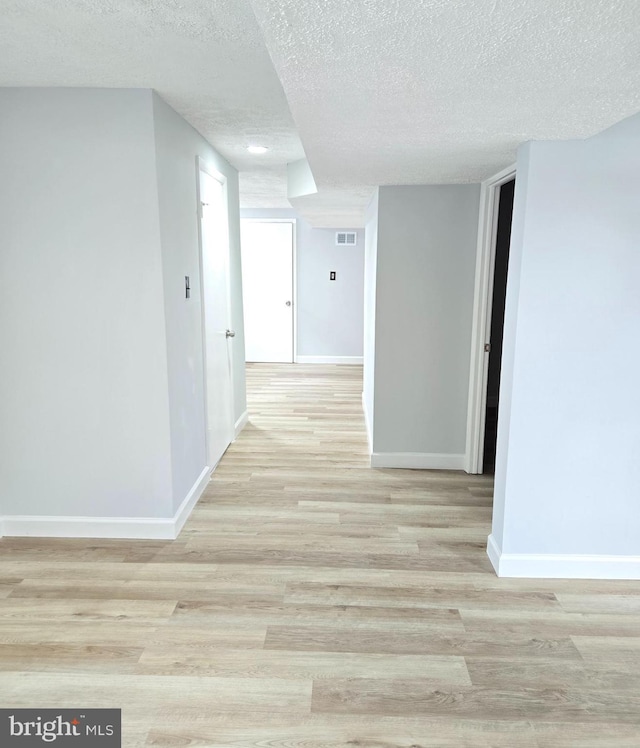 hallway with light hardwood / wood-style floors and a textured ceiling