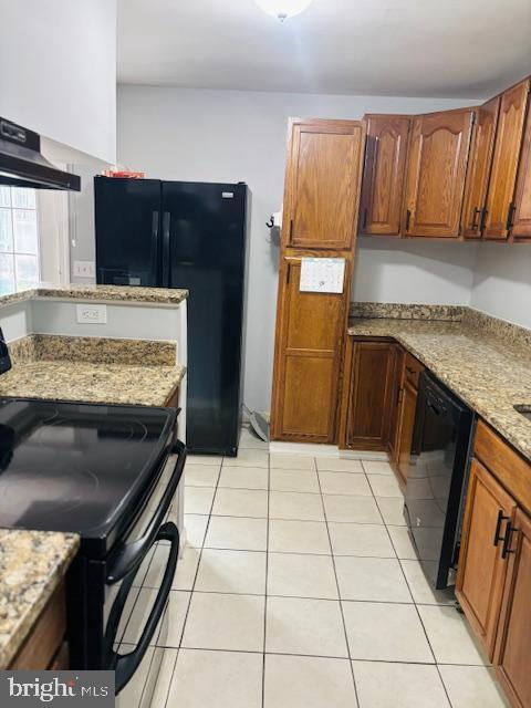 kitchen with light stone counters, light tile patterned floors, wall chimney exhaust hood, black appliances, and brown cabinetry
