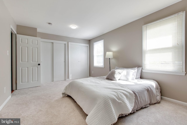 bedroom with two closets, baseboards, and carpet