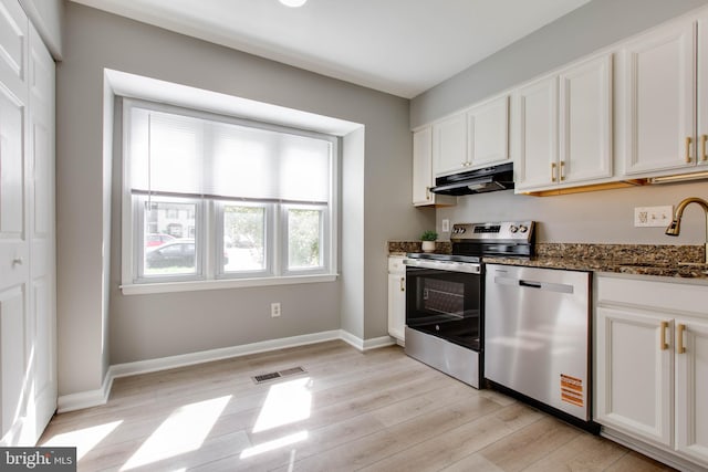 kitchen featuring dark stone countertops, a sink, stainless steel appliances, light wood-style flooring, and under cabinet range hood