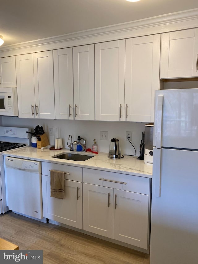 kitchen with sink, white cabinets, light stone counters, light hardwood / wood-style floors, and white appliances