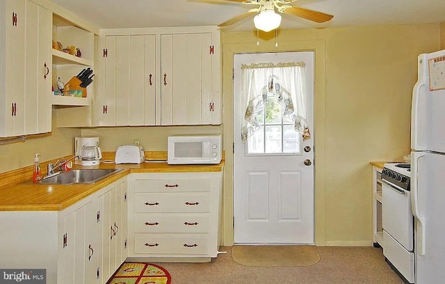 kitchen with sink, white appliances, light colored carpet, ceiling fan, and white cabinets