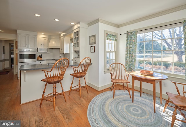 kitchen featuring a kitchen bar, stainless steel oven, kitchen peninsula, light hardwood / wood-style floors, and white cabinets