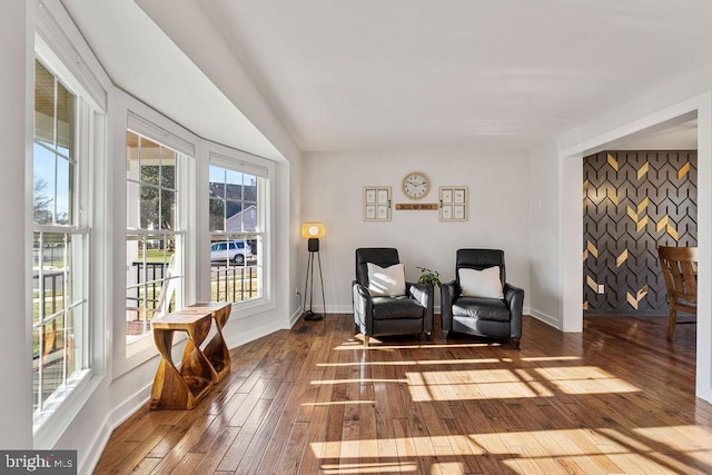 sitting room featuring baseboards, an accent wall, wood finished floors, and lofted ceiling