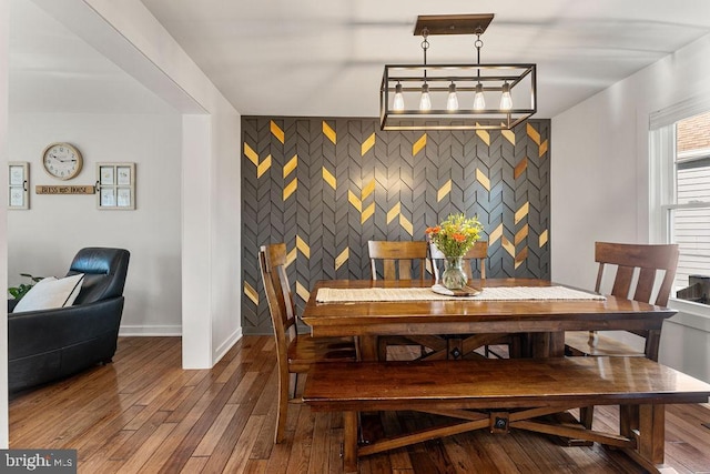 dining space with baseboards, an accent wall, and wood finished floors