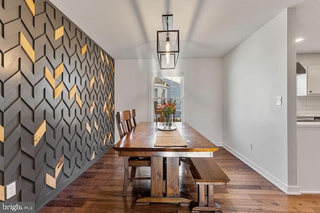 dining room featuring baseboards, dark wood-style floors, and an accent wall