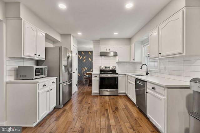 kitchen with appliances with stainless steel finishes, light countertops, under cabinet range hood, white cabinets, and dark wood-type flooring