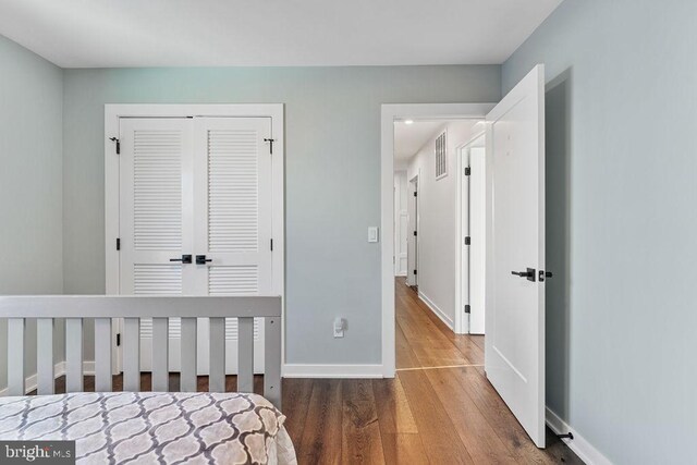 bedroom with a closet, baseboards, wood finished floors, and visible vents