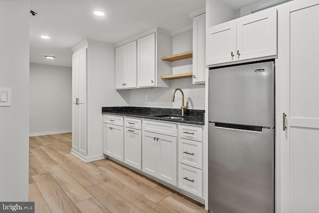 kitchen featuring a sink, freestanding refrigerator, dark stone counters, white cabinets, and open shelves