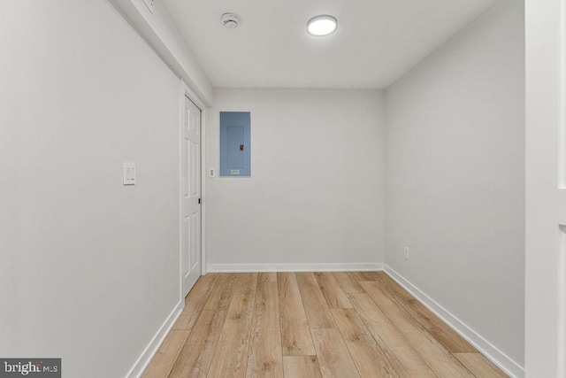 empty room with electric panel, baseboards, and light wood-type flooring