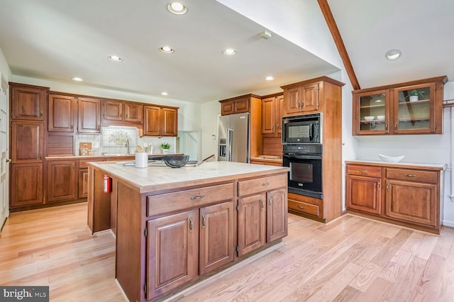 kitchen featuring sink, tasteful backsplash, a center island, light hardwood / wood-style flooring, and black appliances