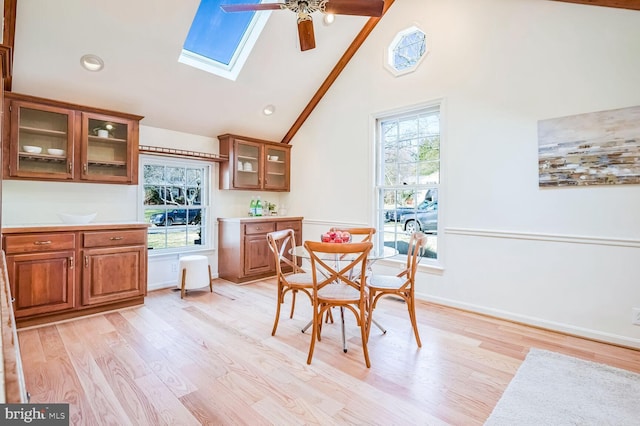 dining area featuring ceiling fan, high vaulted ceiling, light wood-type flooring, and a skylight