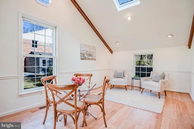 dining room with a skylight, high vaulted ceiling, and light hardwood / wood-style flooring