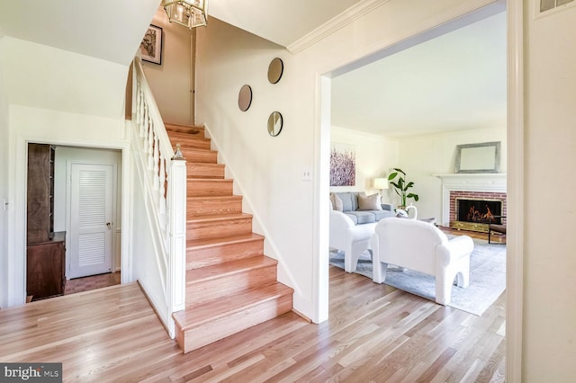 staircase with hardwood / wood-style flooring, ornamental molding, and a brick fireplace