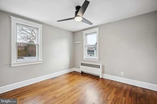 spare room featuring hardwood / wood-style flooring, ceiling fan, radiator heating unit, and plenty of natural light