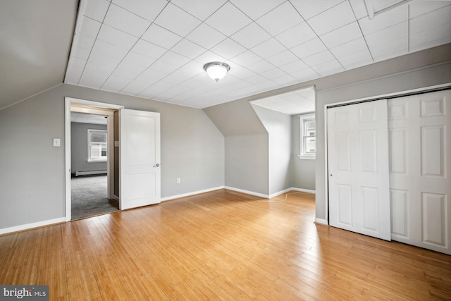 additional living space featuring baseboard heating, vaulted ceiling, and light hardwood / wood-style floors