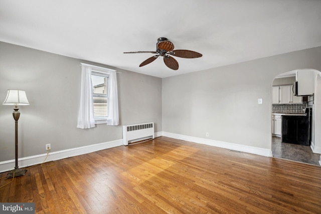 unfurnished living room with ceiling fan, radiator heating unit, and wood-type flooring