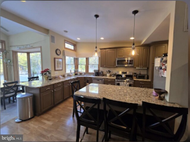 kitchen with appliances with stainless steel finishes, a kitchen breakfast bar, kitchen peninsula, and light stone countertops
