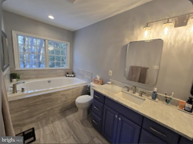 bathroom featuring vanity, tiled bath, and toilet