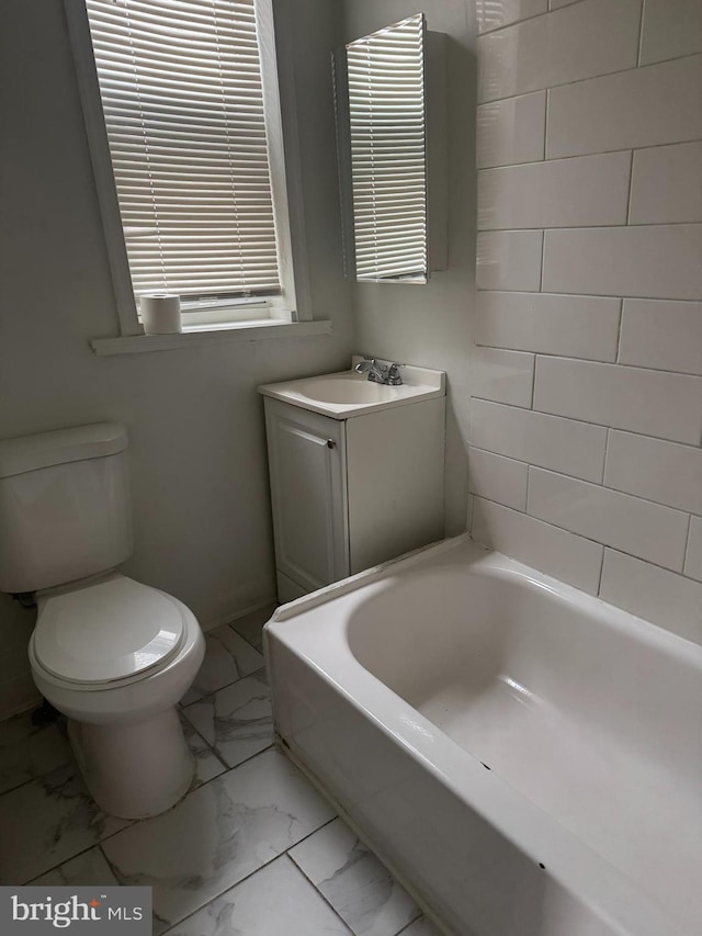 bathroom featuring toilet, marble finish floor, a bathtub, and vanity