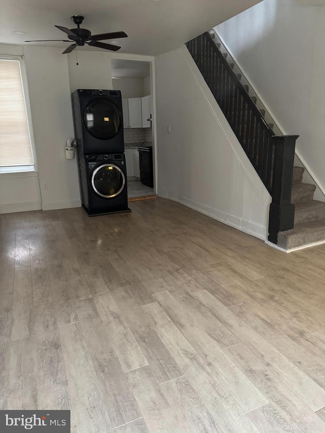 unfurnished living room featuring a ceiling fan, wood finished floors, stacked washer and clothes dryer, and stairs