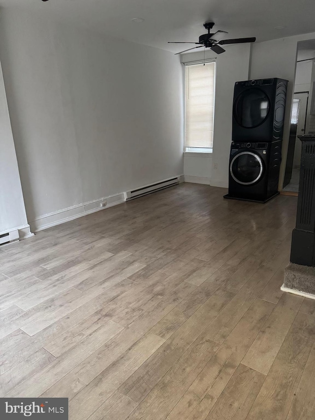 unfurnished living room with a baseboard heating unit, stacked washer / dryer, a ceiling fan, and wood finished floors