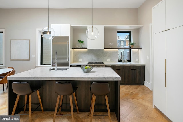 kitchen featuring a breakfast bar, light parquet floors, dark brown cabinetry, an island with sink, and white cabinets