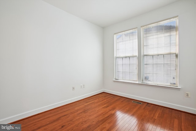 spare room with wood-type flooring, visible vents, and baseboards