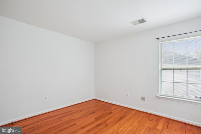 spare room with light wood finished floors, visible vents, and baseboards