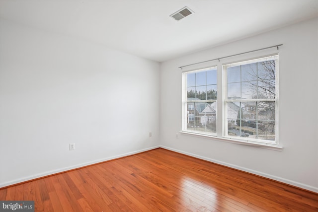 empty room with baseboards, visible vents, and hardwood / wood-style floors