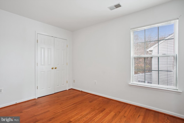 unfurnished bedroom featuring a closet, wood finished floors, visible vents, and baseboards