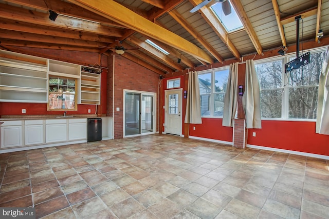 unfurnished sunroom with ceiling fan, lofted ceiling with skylight, and a sink