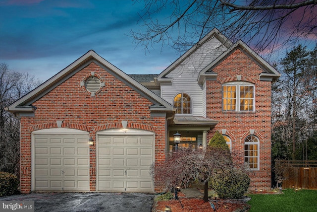 traditional-style house featuring driveway, brick siding, an attached garage, and fence