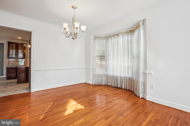 unfurnished room with a chandelier, ornamental molding, light wood-style flooring, and baseboards