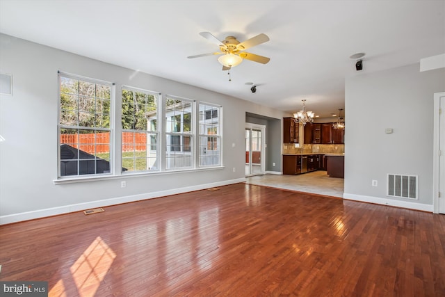 unfurnished living room with ceiling fan with notable chandelier, hardwood / wood-style flooring, visible vents, and baseboards