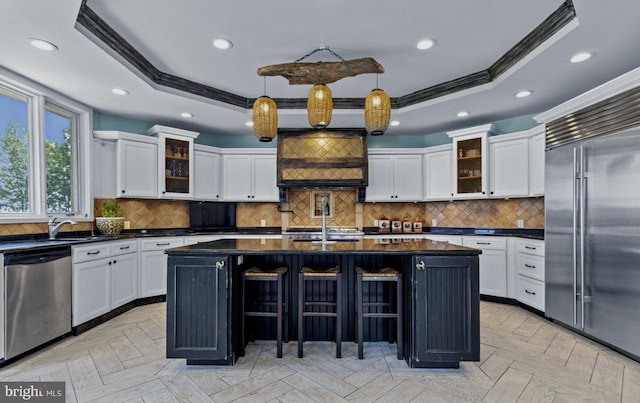 kitchen featuring a center island with sink, appliances with stainless steel finishes, a tray ceiling, pendant lighting, and light parquet floors