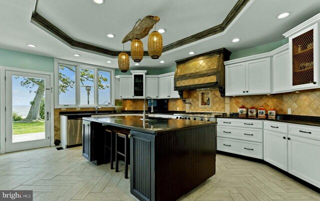 kitchen featuring sink, hanging light fixtures, a center island with sink, a tray ceiling, and light parquet floors