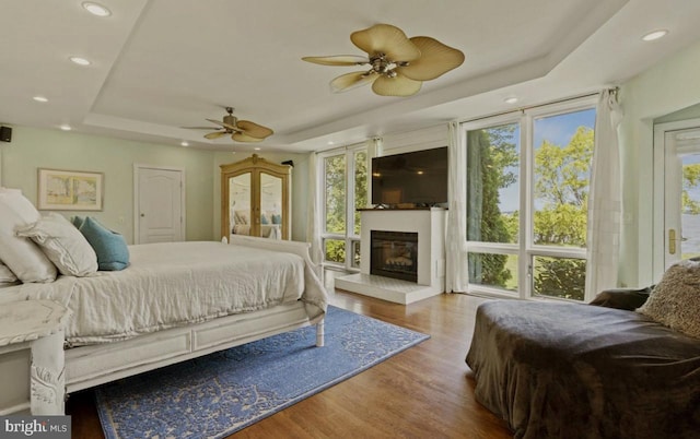 bedroom with ceiling fan, a large fireplace, a raised ceiling, and hardwood / wood-style floors