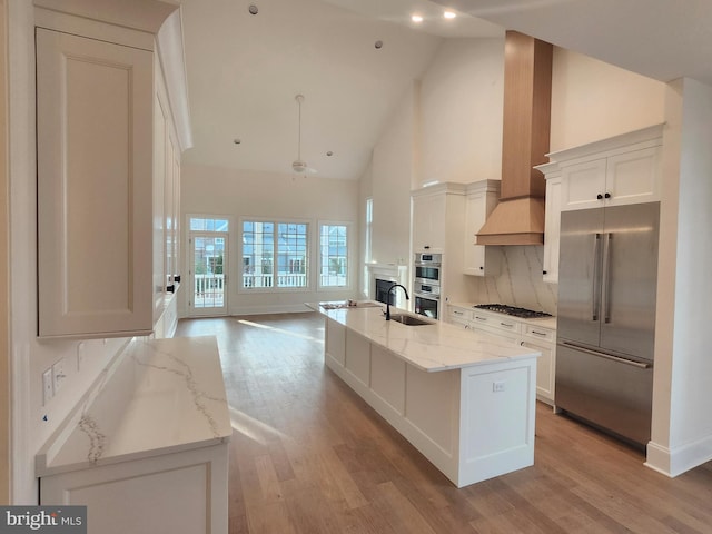 kitchen featuring appliances with stainless steel finishes, sink, white cabinets, a kitchen island with sink, and light stone counters