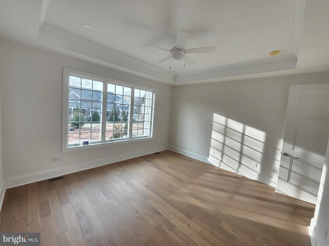 empty room with a raised ceiling, ceiling fan, and light wood-type flooring