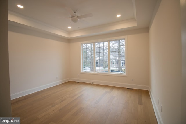 empty room with ceiling fan, ornamental molding, a tray ceiling, and light hardwood / wood-style flooring