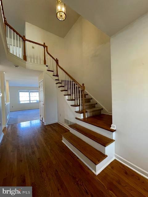 staircase featuring a high ceiling, hardwood / wood-style floors, and an inviting chandelier