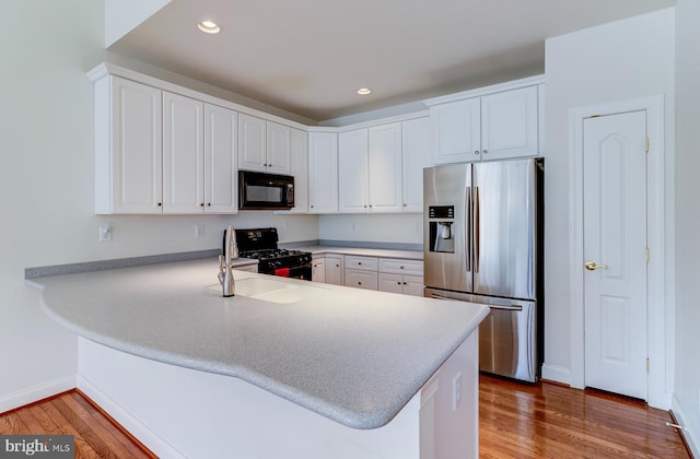 kitchen featuring black appliances, sink, white cabinets, light hardwood / wood-style floors, and kitchen peninsula