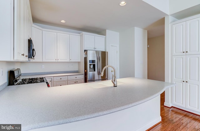 kitchen with stainless steel fridge, white cabinetry, light hardwood / wood-style floors, range with gas stovetop, and kitchen peninsula