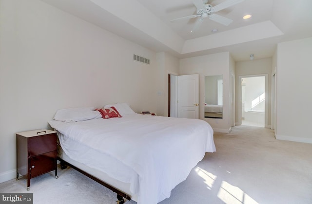 bedroom with a raised ceiling, connected bathroom, light carpet, and ceiling fan