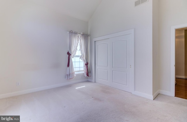 unfurnished bedroom featuring a closet, high vaulted ceiling, and light carpet