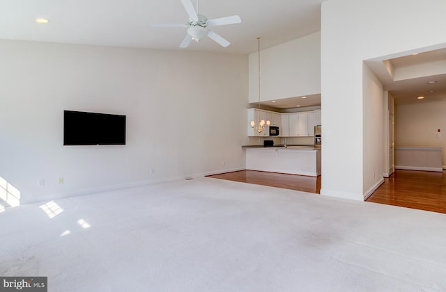 unfurnished living room featuring light carpet, high vaulted ceiling, and ceiling fan