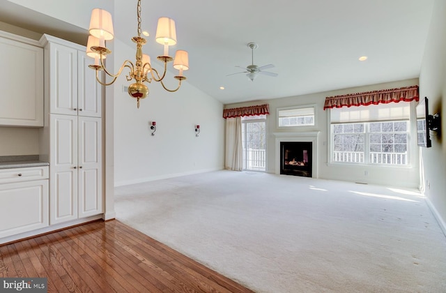 unfurnished living room featuring ceiling fan with notable chandelier, light colored carpet, and lofted ceiling