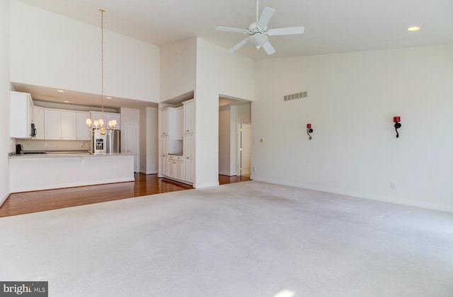 unfurnished living room with dark carpet, high vaulted ceiling, and ceiling fan with notable chandelier